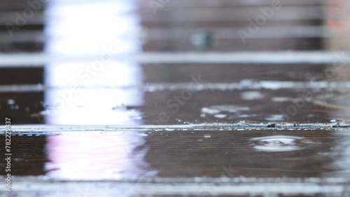 Texture of a terrace board with reflection highlights on it. Slowly dripping raindrops create a lot of splashes on the surface.