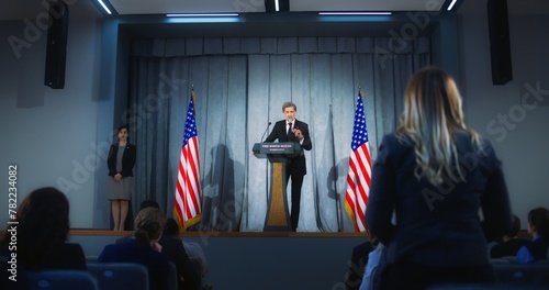 Confident American republican politician delivers successful speech to supporters at government election rally. New president of USA gives interview for media. Backdrop with American flags. Zoom out. photo