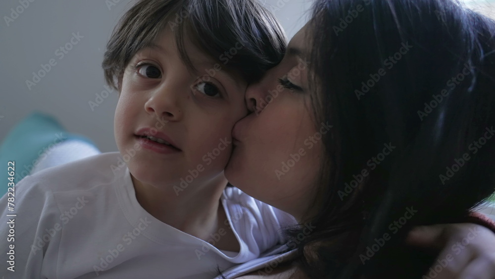 Mother and child healthy caring relationship in relaxing afternoon seated on couch at home, parent kissing son's cheek in display of love and affection Mother and child healthy caring relationship in relaxing afternoon seated on couch at home, parent kissing son's cheek in display of love and affection