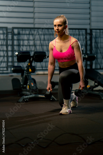 in the gym a girl with a ponytail in a pink top does lunges with dumbbells in her hands