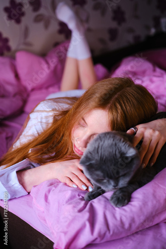 pretty young ginger woman with her gray british cat in pink bed at home girl in white shirt hug the cat