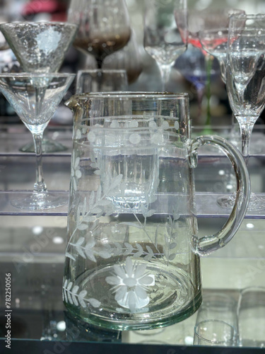A pitcher with a floral design sits on a table next to a variety of glasses