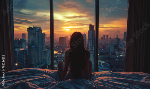 back view of young woman wake up at luxury hotel room or apartment, person by panoramic window, city and skyscrapers