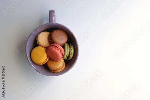 Purple cup filled with pastel macarons on white background. Top view.