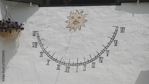 Sundial with hours painted on wall with wooden stick shadow indicating the time of the day, an old rustic solar clock on whitewashed wall of a house in Binibeca Vell, Menorca, Spain