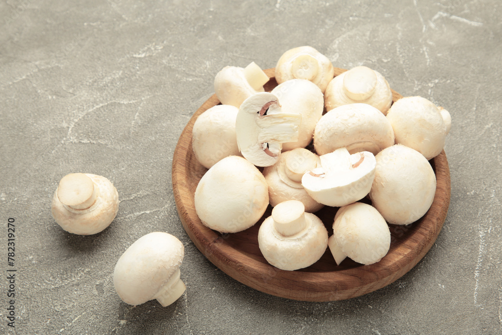 Fresh white champignon mushrooms on wooden plate on grey background. Fresh white champignon mushrooms on wooden plate on grey background.