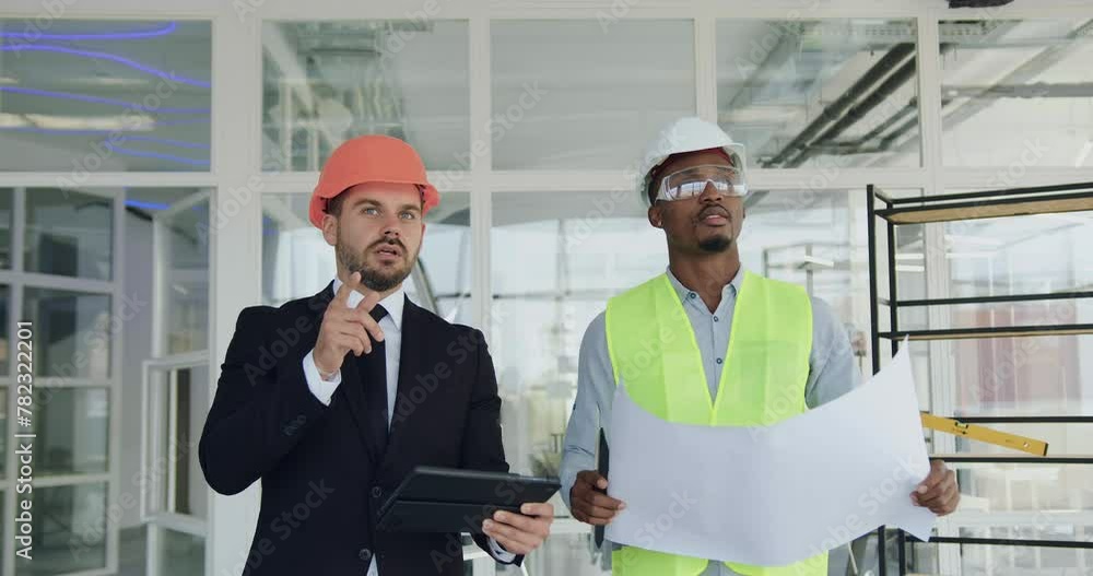 Portrait of man main manager with professional african american engineer in unfinished office building and discussing project details. Building industry concept. Portrait of man main manager with professional african american engineer in unfinished office building and discussing project details. Building industry concept.