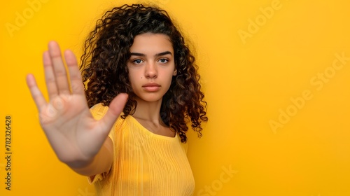 A woman making a stop sign gesture with her hand against an isolated yellow background. photo