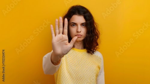 A woman making a stop sign gesture with her hand against an isolated yellow background. photo