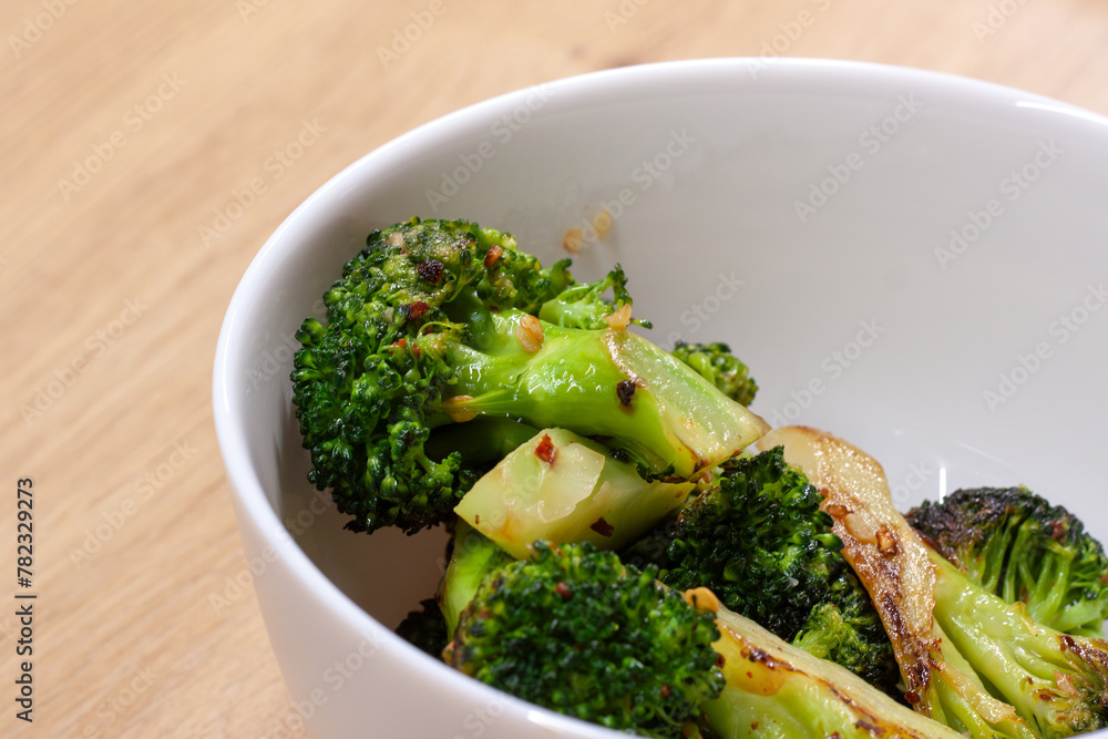 The white bowl with stir-fried broccoli on the wooden table 