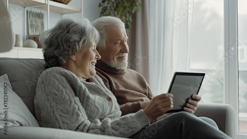 a senior couple as they happily engage with a tablet computer while seated on a cozy sofa in their sunlit living room, radiating warmth and companionship.