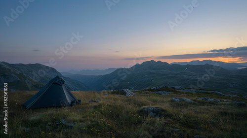 a man in a hat sits on a hill in the mountains