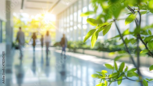 Blurred background of people walking in modern office building with green plants and sunlight