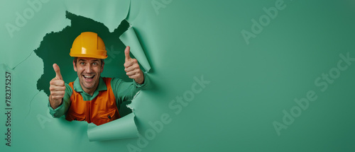 A smiling construction worker in green giving a thumbs up through a paper tear
