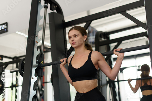 fit woman does barbell squats in Smith machine in fitness gym