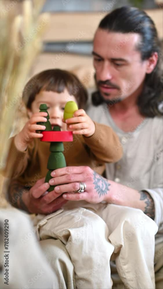 Father playing with his son with colourful, ecological wooden toys in a barn, near square hay bales Father playing with his son with colourful, ecological wooden toys in a barn, near square hay bales