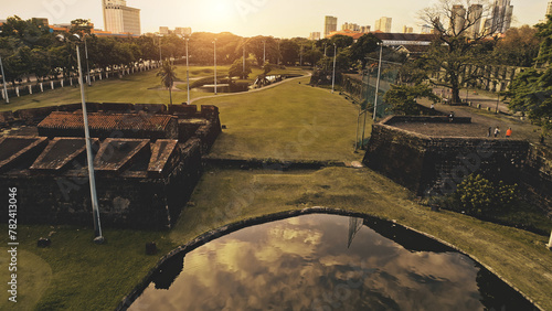 Pond with sun reflection at designed green park aerial. Green grass valey with lake at path. Urban greenery at road side of downtown streets. Philippines capital city of Manila at cinematic sunlight photo