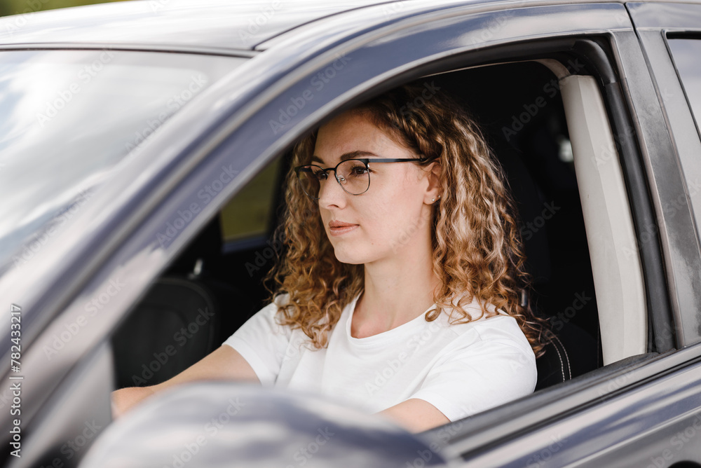 young confident woman driving car in summer , attractive caucasian woman in white t-shirt , attractive caucasian woman in white t-shirt