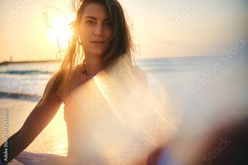A woman poses with the sun setting at her back, creating a beautiful lens flare and silhouette effect on the beach