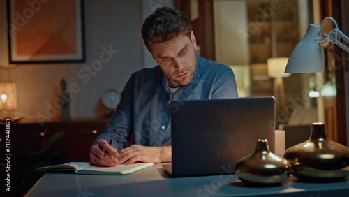 Online student studying night home looking laptop closeup. Man making notes