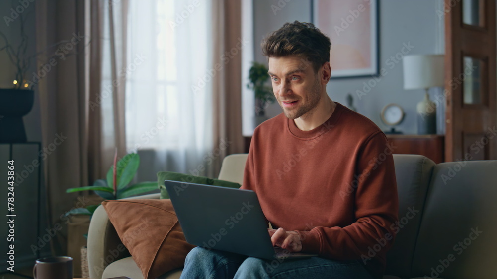 Smiling hipster chatting laptop on couch. Happy man freelancer working remotely Smiling hipster chatting laptop on couch. Happy man freelancer working remotely
