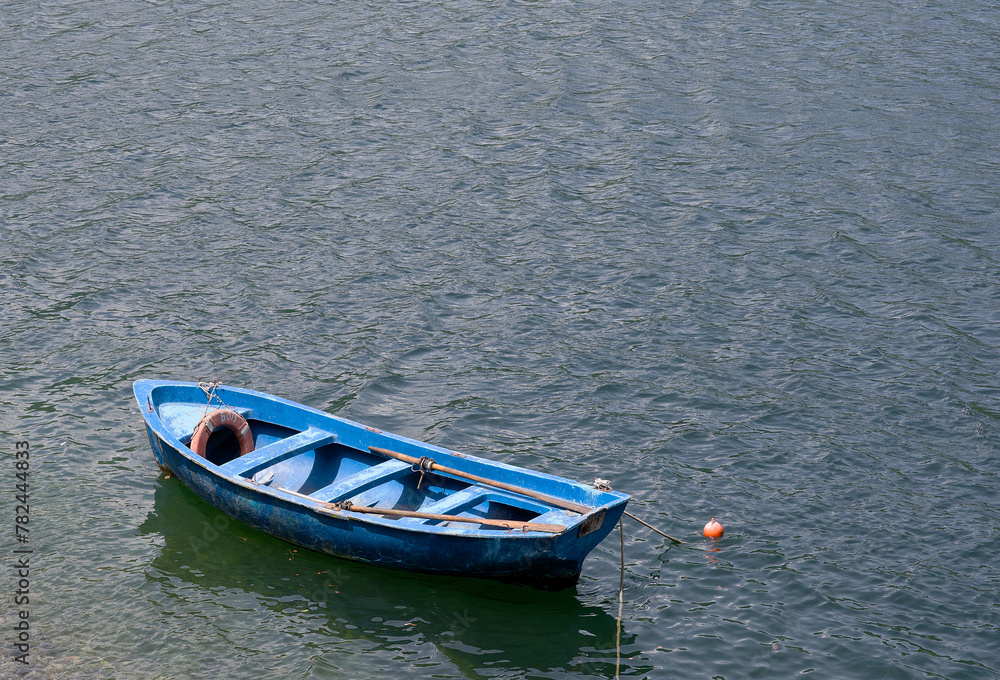 A blue colored wooden boat floats on the water in windy sunny weather.