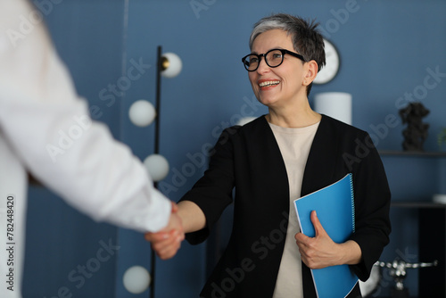 professional portrait, a smiling businesswoman confidently shakes hands, surrounded by paperwork and exuding success. © Andrii Zastrozhnov