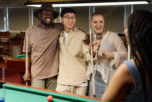 Waist up portrait of multiethnic group of friends chatting and smiling while enjoying game of pool together in low light