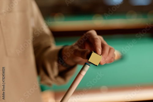 Close up of unrecognizable man using chalk cube on cue stick while playing pool copy space