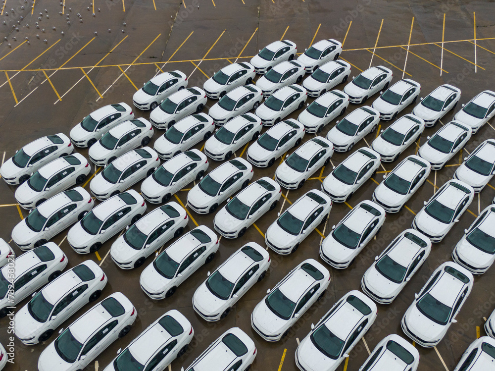 Fototapeta premium A large parking lot full of white cars. Cars leaving the car factory are waiting at the port for sale and transportation.