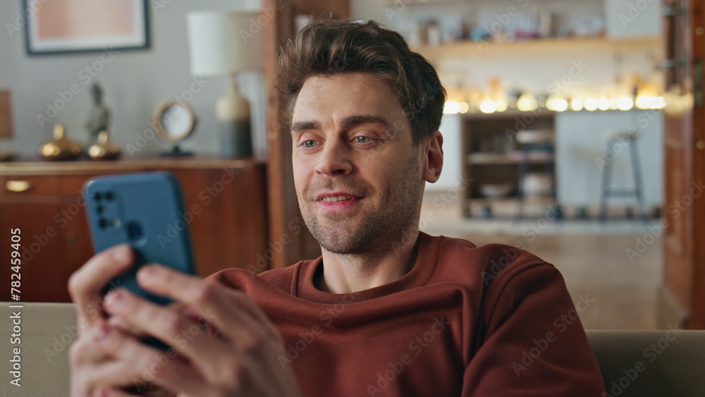 Smiling guy looking mobile phone screen on couch closeup. Man reading message Smiling guy looking mobile phone screen on couch closeup. Man reading message