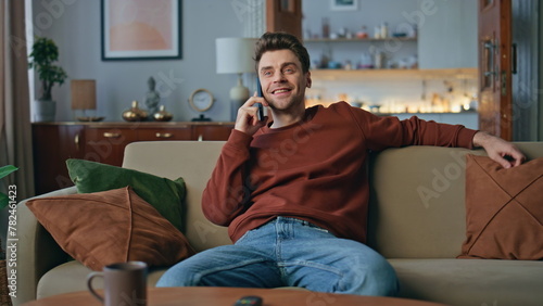 Resting guy communicating smartphone at cozy couch. Happy man talking cellphone