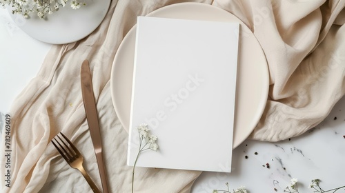Elegant table setting mockup with white empty plate, cutlery, and a blank menu card. Flat lay composition for restaurant branding or event design with copy space © Tatyana