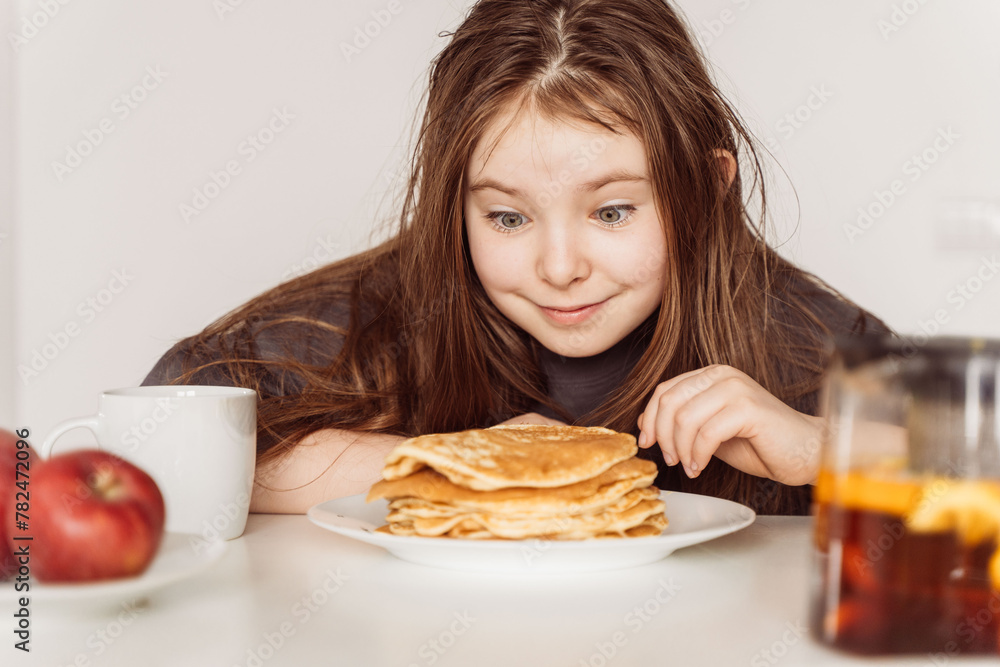 Pre-teen Girl looks at a stack of pancakes with the desire to eat them. High quality photo Pre-teen Girl looks at a stack of pancakes with the desire to eat them. High quality photo