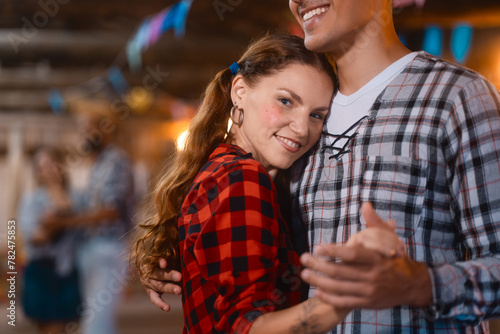 Affectionate young woman in checkered attire dancing closely with her partner at a Festa Junina. Intimate couple in festive garb enjoying the rhythm of a traditional Brazilian dance