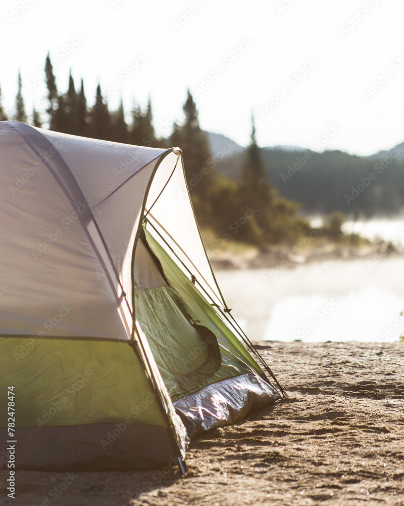 Fototapeta premium Green camping tent in the morning light with lake, mountains and trees in the background