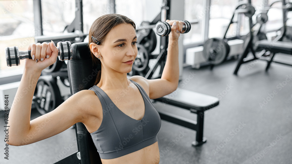 young athletic caucasian woman trains in fitness gym, doing dumbbell press up on bench, brunette girl in grey top and leggings, healthy lifestyle concept young athletic caucasian woman trains in fitness gym, doing dumbbell press up on bench, brunette girl in grey top and leggings, healthy lifestyle concept