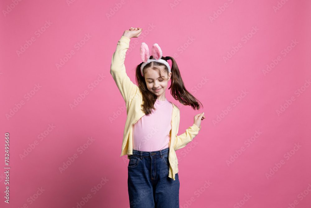 Energetic and positive kid dancing in studio while wearing bunny ears in excitement of Easter Sunday celebrations. Pleased carefree youngster who displays comfort in her dance skills. Energetic and positive kid dancing in studio while wearing bunny ears in excitement of Easter Sunday celebrations. Pleased carefree youngster who displays comfort in her dance skills.