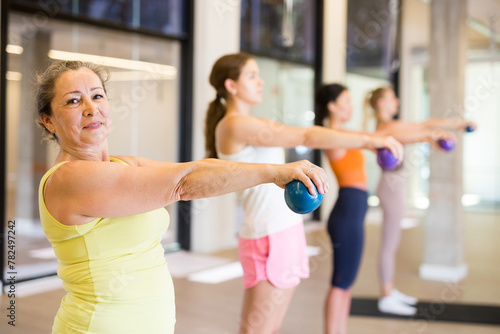 Women holding dumbbells in each hand and doing exercises in fitness room