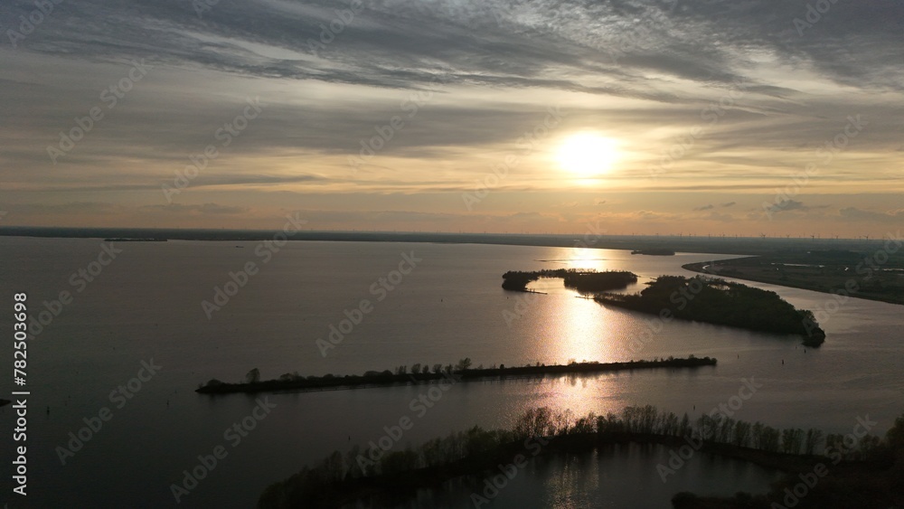 Scenic aerial view of a tranquil lake at sunset with islands and peninsulas, silhouetted against the golden sky reflected in the calm water.