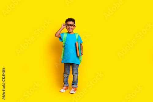 Full length photo of sweet excited preteen boy wear blue t-shirt spectacles walking school empty space isolated yellow color background
