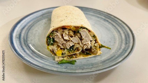 small fried pieces of chicken meat with vegetables, corn wrapped in pita bread on a gray plate on a white table and side view. Healthy snack healthy food