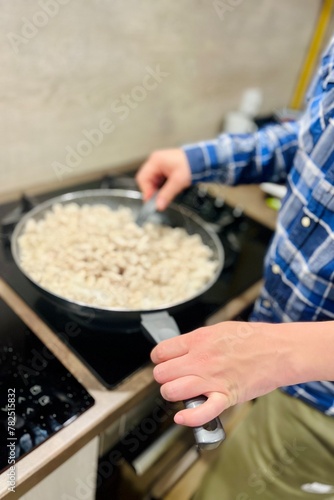 the process of frying pieces of chicken breast in a black frying pan on an induction cooker. female hands holding a frying pan. kitchen