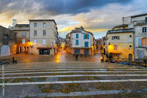 Illuminated shops and cafes after an evening rain seen from the steps of the ancient arena in the historic medieval old town of Arles, France, in the Provence region.