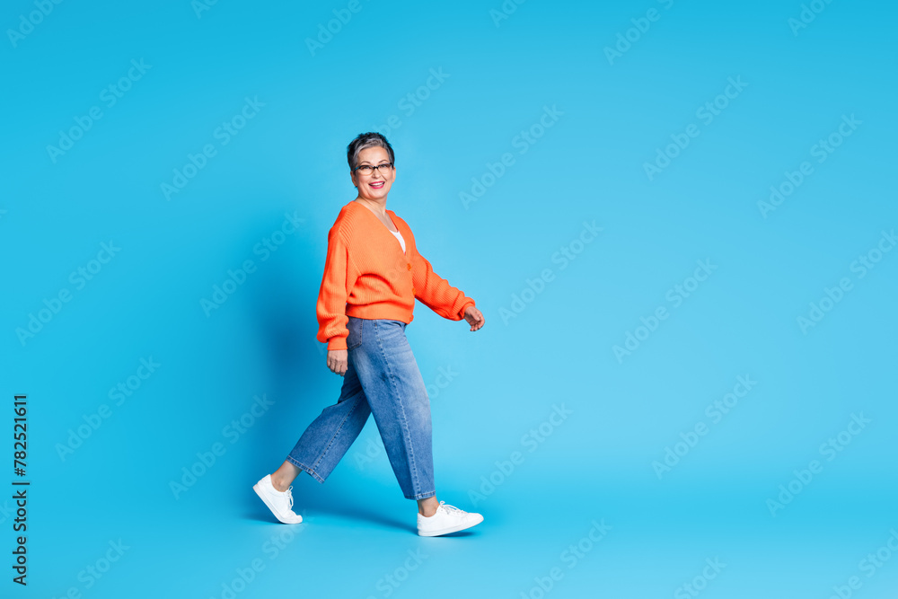 Full body photo of lovely senior lady walking shopping dressed stylish orange garment isolated on blue color background