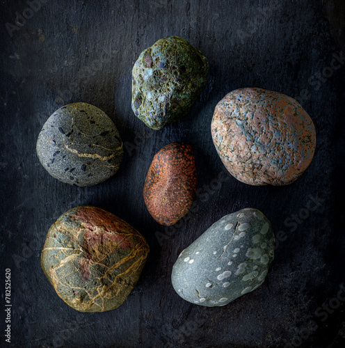 Six rocks on slate surface and light-painted from the side.