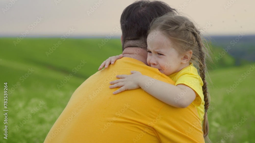 Baby daughter crying in park in arms of her father. Dad hugs, reassures
