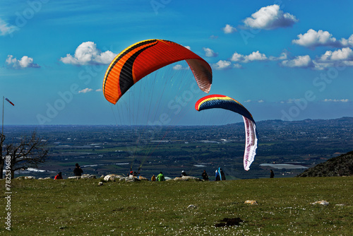 People enjoy the extreme sport of paragliding. Outdoor living in the blue sky. Incredible nature and views. Adventures and adrenaline with parachute. Travel destination Norma Latina Italy. Summer 