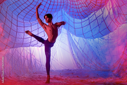 male ballet dancer in a outfit is dancing in front of a blue background.