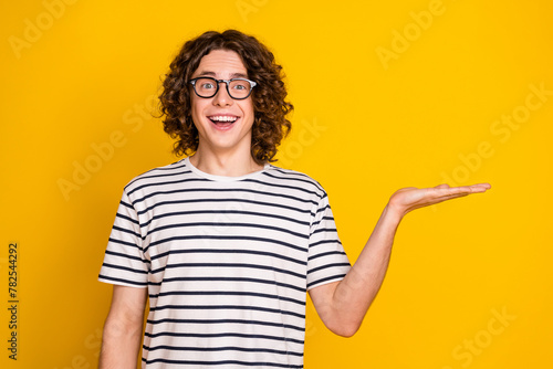 Photo portrait of pretty teen male palm hold empty space billboard wear trendy striped outfit isolated on yellow color background